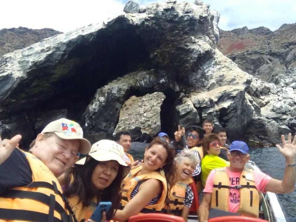 Grupo con chalecos salvavidas en un bote frente a un arco de roca en la Reserva Nacional Pingüino de Humboldt